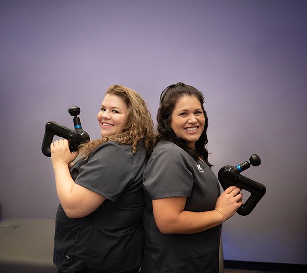 Two massage therapists back to back with massage guns