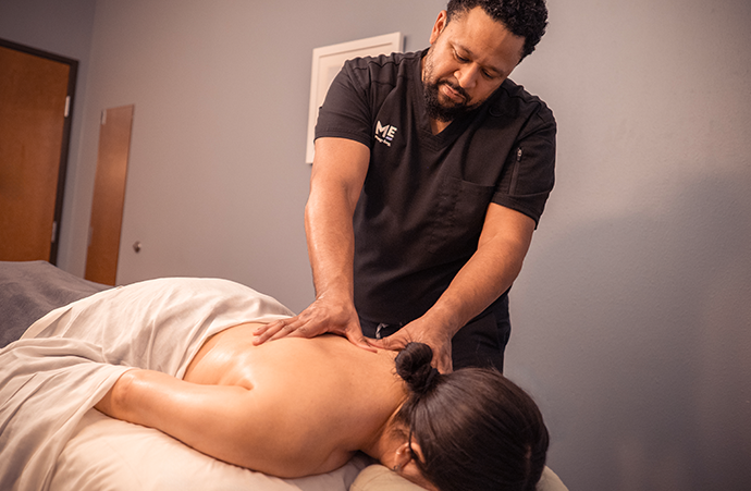 Massage therapist massaging customer's back as she lies on table. 
