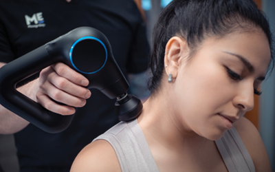 Woman relaxes at massage gun is moved along her shoulders. 