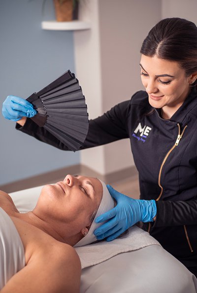 Woman laying on table as esthetician waves fan above her face. 