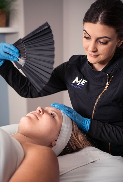Woman laying on table as esthetician waves fan above her face. 