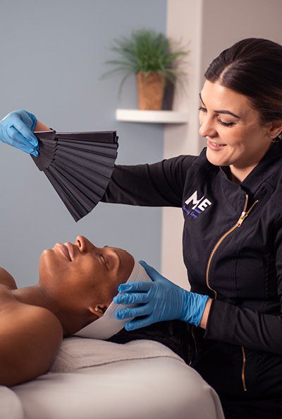 Woman laying on table as esthetician waves fan above her face. 