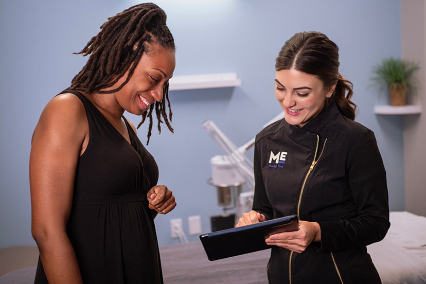 Client and esthetician smiling as they look down at tablet device. 