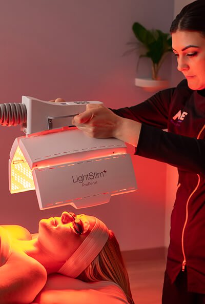 Esthetician standing above a woman as she receives LED Light Therapy during a Calming Nourishing Light Treatment. 