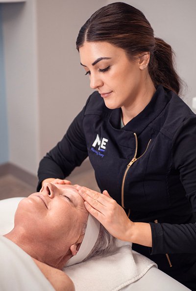 Esthetician providing an age-defying facial to woman laying down with her eyes closed. 