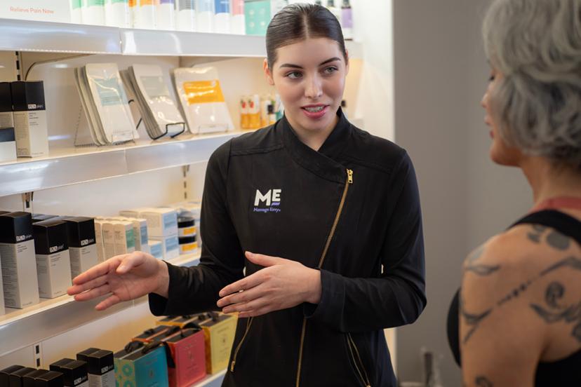 Massage Envy esthetician pointing at available skin care products on product display. 