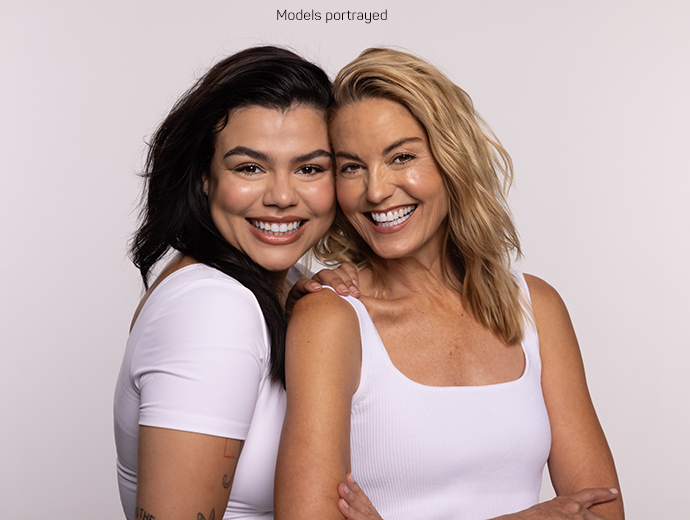 Two women standing next to each other and smiling brightly. 