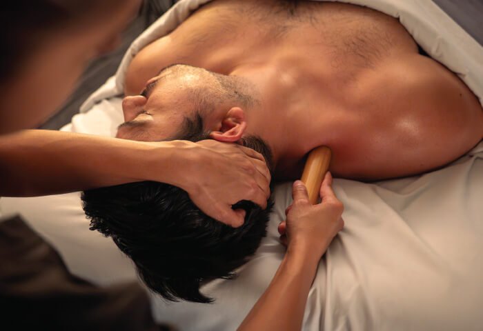 Therapist massaging man's shoulder with bamboo stick. 
