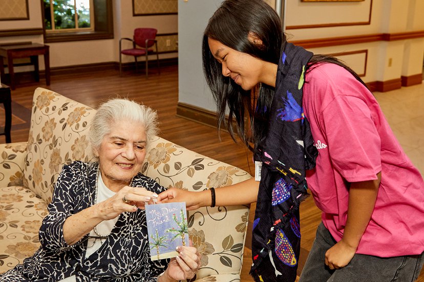 Woman handing holiday card to senior sitting down on couch. 