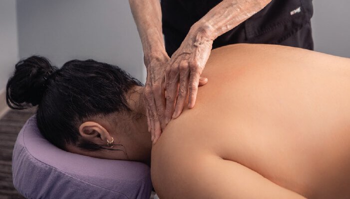 Woman with her face down as she receives shoulder massage from therapist. 