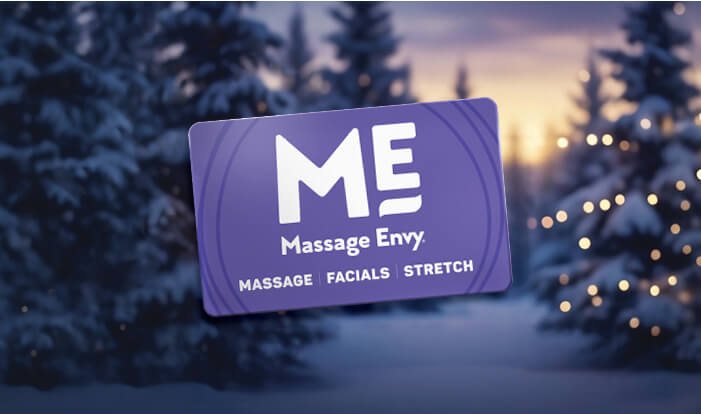 Massage Envy gift card placed in front of a winter background with Christmas trees. 
