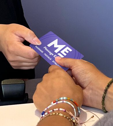 Close-up of associate handing Massage Envy gift card to customer. 