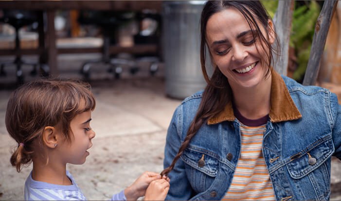 Daughter braiding her mom's hair while the mom smiles. 