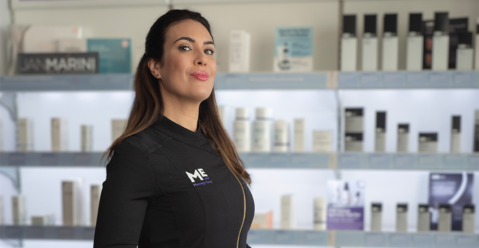 Esthetician smilin as she stands in front of product display. 