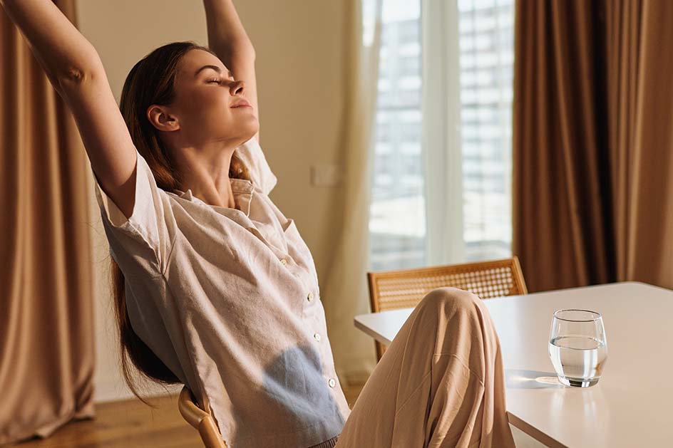 Woman sitting on chair as she stretches our her arms up over her head. 
